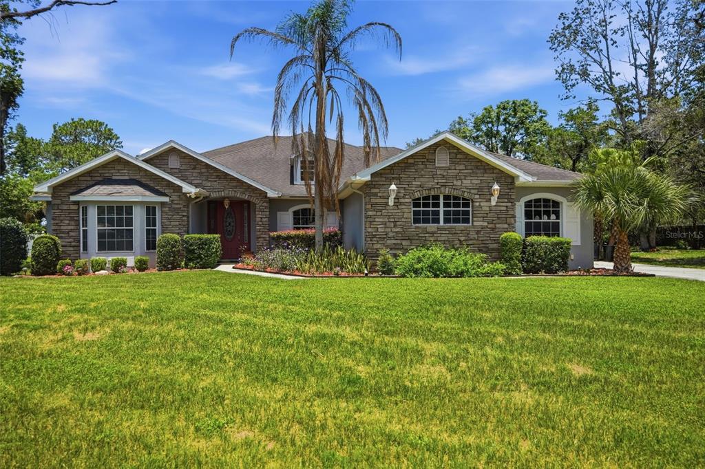 A single-story house with a stone facade, a front lawn, and palm trees — 9011 FOXDALE LANE, SPRING HILL, FL