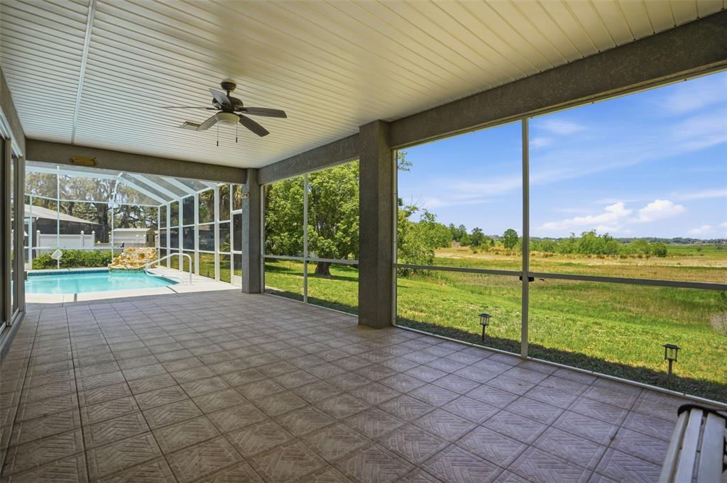 A covered, tiled patio with a ceiling fan overlooks a swimming pool and grassy field — 9011 FOXDALE LANE, SPRING HILL, FL