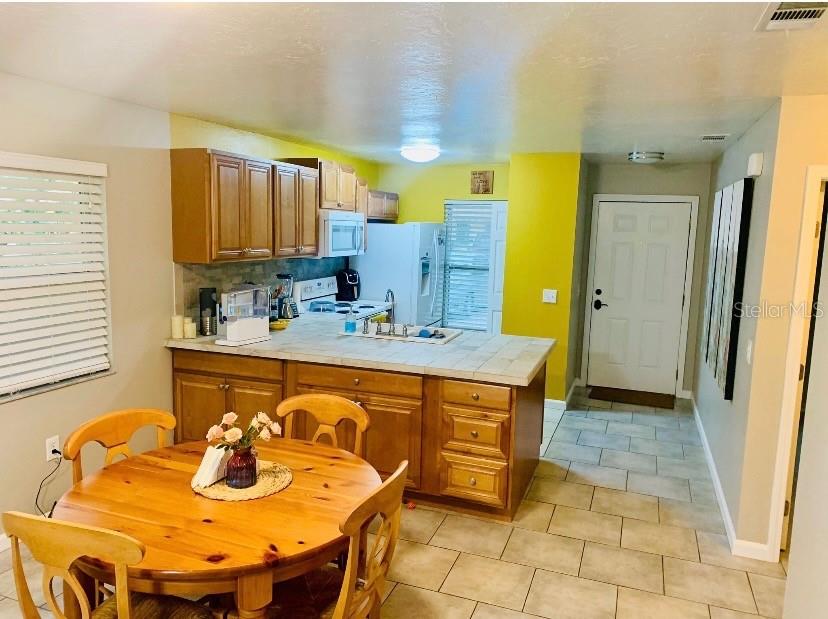 A kitchen with wood cabinets and a tile countertop overlooks a round wooden dining table — 4643 SUMMERWIND DRIVE UNIT 22, SARASOTA, FL