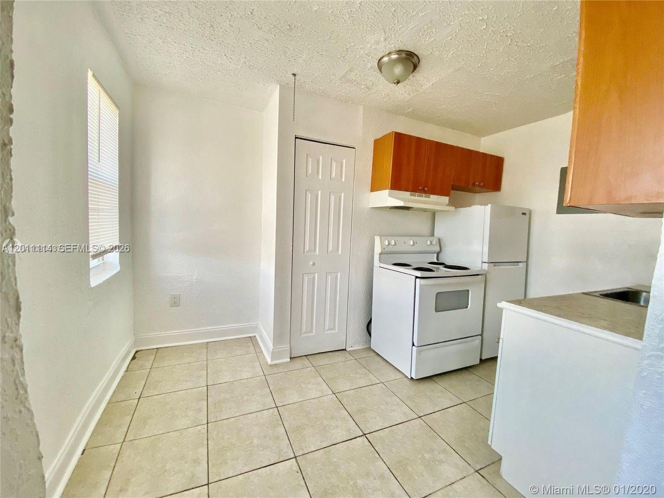 A small kitchen features white tile floors, white appliances, and wood-toned upper cabinets — 50 NW 79th St # 9, Miami FL 33150, MIAMI, FL