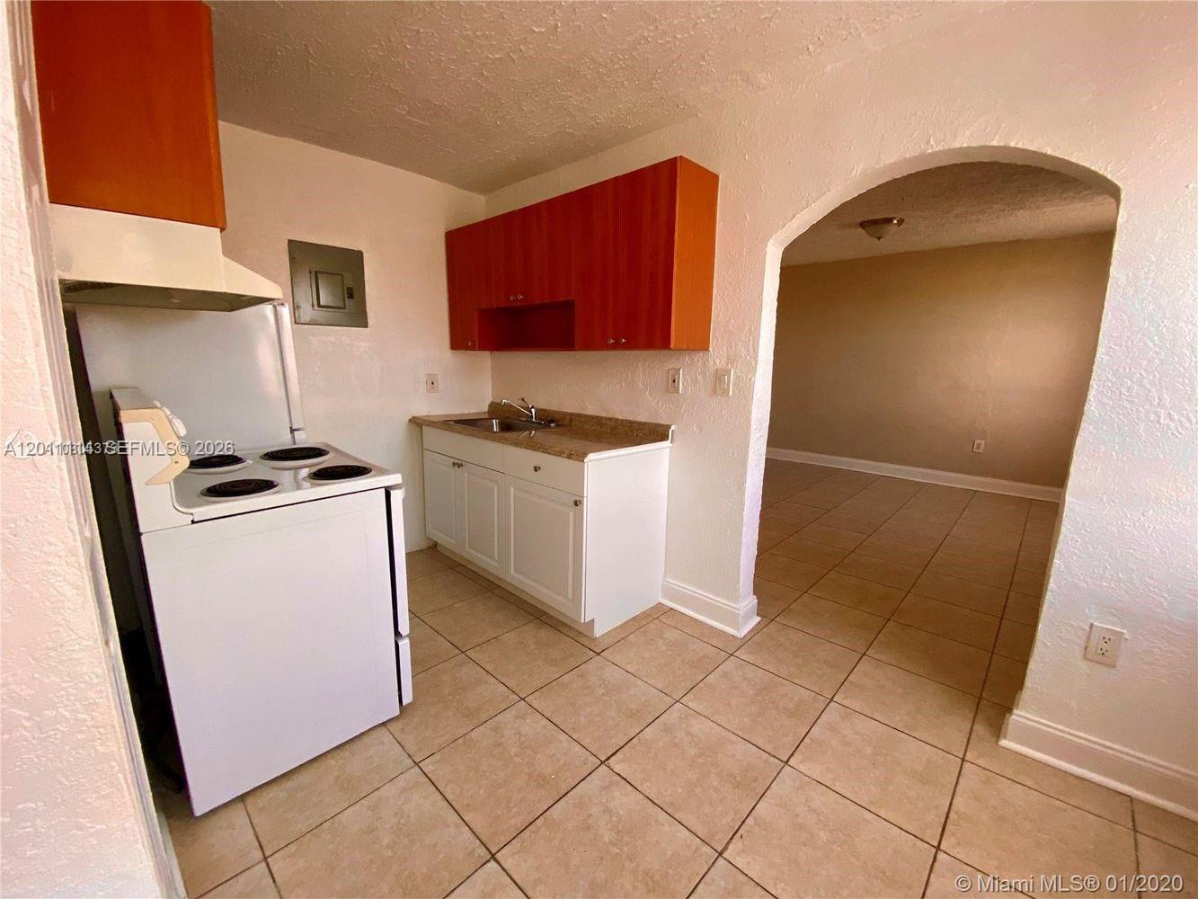 A kitchen with white cabinets, a white stove, and tile flooring leads into an adjacent room — 50 NW 79th St # 9, Miami FL 33150, MIAMI, FL
