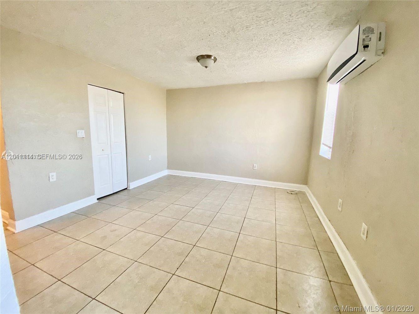 An empty room features beige walls, light-colored tile flooring, a white closet door, and a wall-mounted air conditioner — 50 NW 79th St # 9, Miami FL 33150, MIAMI, FL