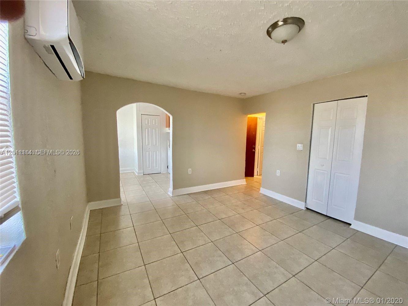 A room with beige walls, tile flooring, an arched doorway, and white closet doors — 50 NW 79th St # 9, Miami FL 33150, MIAMI, FL