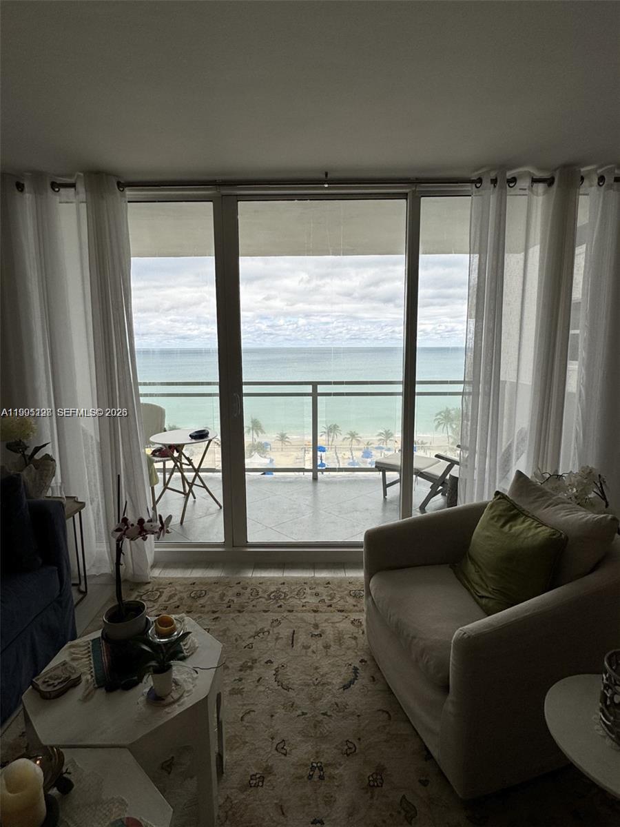 A living room with a beige armchair and rug overlooks a balcony and the ocean — 2030 S Ocean Dr # 815, Hallandale Beach FL 33009, HALLANDALE BEACH, FL
