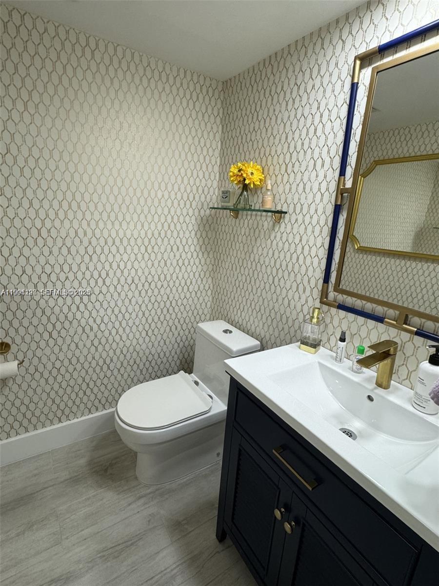 A bathroom features patterned wallpaper, a dark vanity with a gold faucet, and a mirror — 2030 S Ocean Dr # 815, Hallandale Beach FL 33009, HALLANDALE BEACH, FL