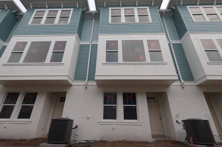A low-angle exterior view of three attached townhomes with blue siding and white stucco bases — 446 31ST WAY N, ST PETERSBURG, FL