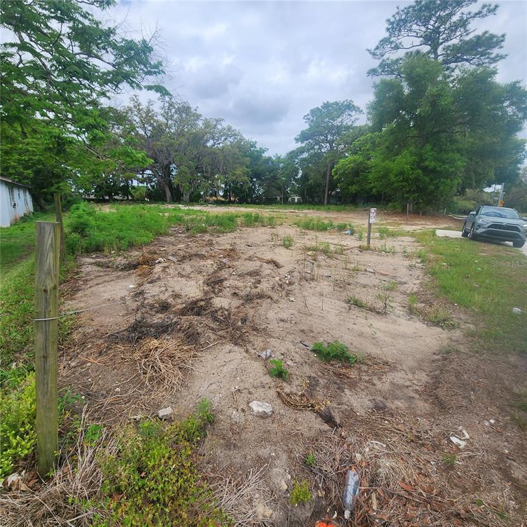 A vacant, sandy residential lot with scattered vegetation and surrounding trees under a cloudy sky — 1648 CLARCONA ROAD, APOPKA, FL
