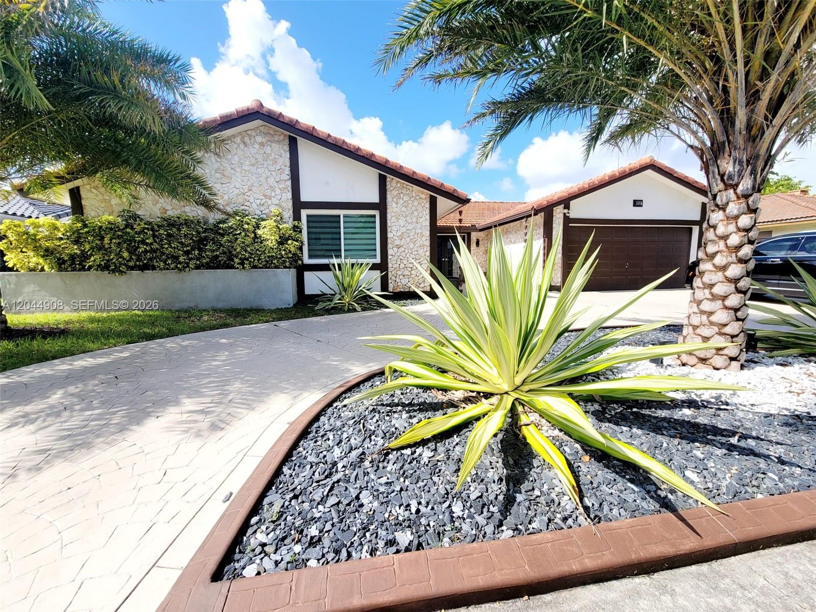 The exterior of a single-story house features stone siding, a tiled roof, and a paved driveway — 6324 NW 201st Ln, Hialeah FL 33015, HIALEAH, FL