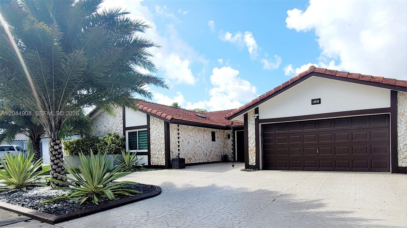 A single-story house features a stone facade, a brown garage door, and a tiled roof — 6324 NW 201st Ln, Hialeah FL 33015, HIALEAH, FL
