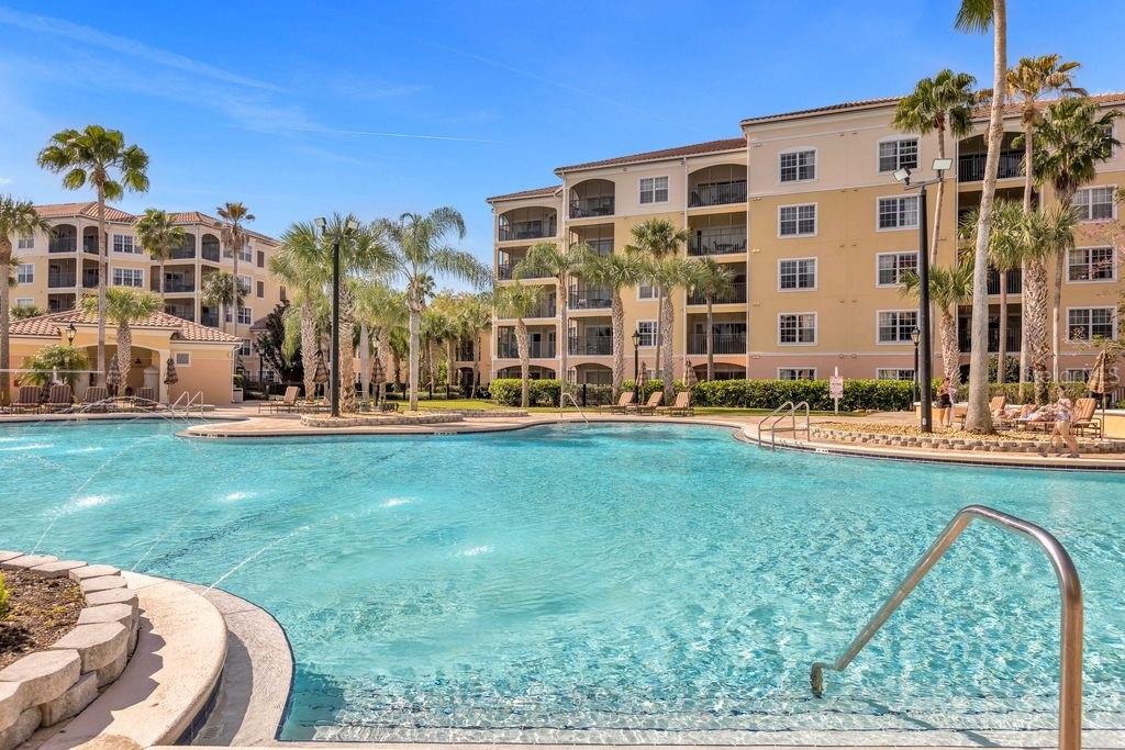 A large swimming pool with fountains sits in front of a multi-story apartment complex — 8762 WORLDQUEST BOULEVARD UNIT 6102, ORLANDO, FL