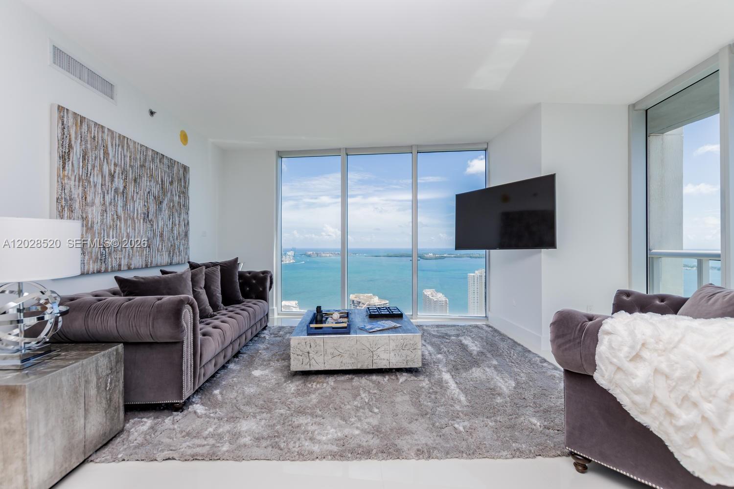 A living room features a grey tufted sofa, a textured coffee table, and floor-to-ceiling ocean views — 495 Brickell Ave # 4901, Miami FL 33131, MIAMI, FL