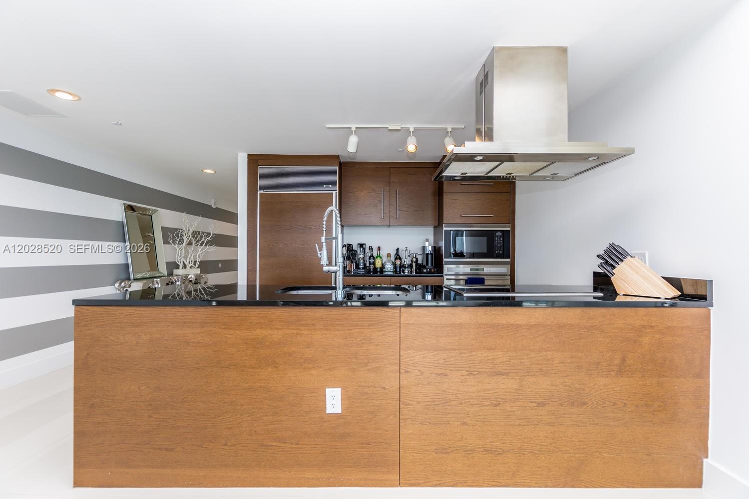 A modern kitchen features a wooden island, black countertops, and stainless steel appliances — 495 Brickell Ave # 4901, Miami FL 33131, MIAMI, FL