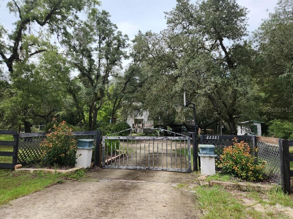 A gated driveway leads to a house partially obscured by large trees and foliage — Lot 27 SW PINE BLUFFS ROAD, DUNNELLON, FL