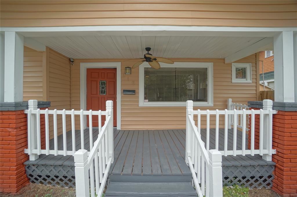 A front porch with a grey wooden deck, white railings, and a red front door — 916 E 25TH AVENUE, TAMPA, FL