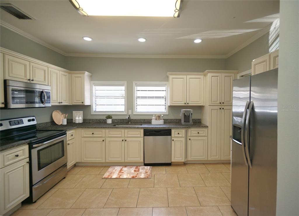 A kitchen with cream-colored cabinets, stainless steel appliances, granite countertops, and light-colored tile flooring — 916 E 25TH AVENUE, TAMPA, FL
