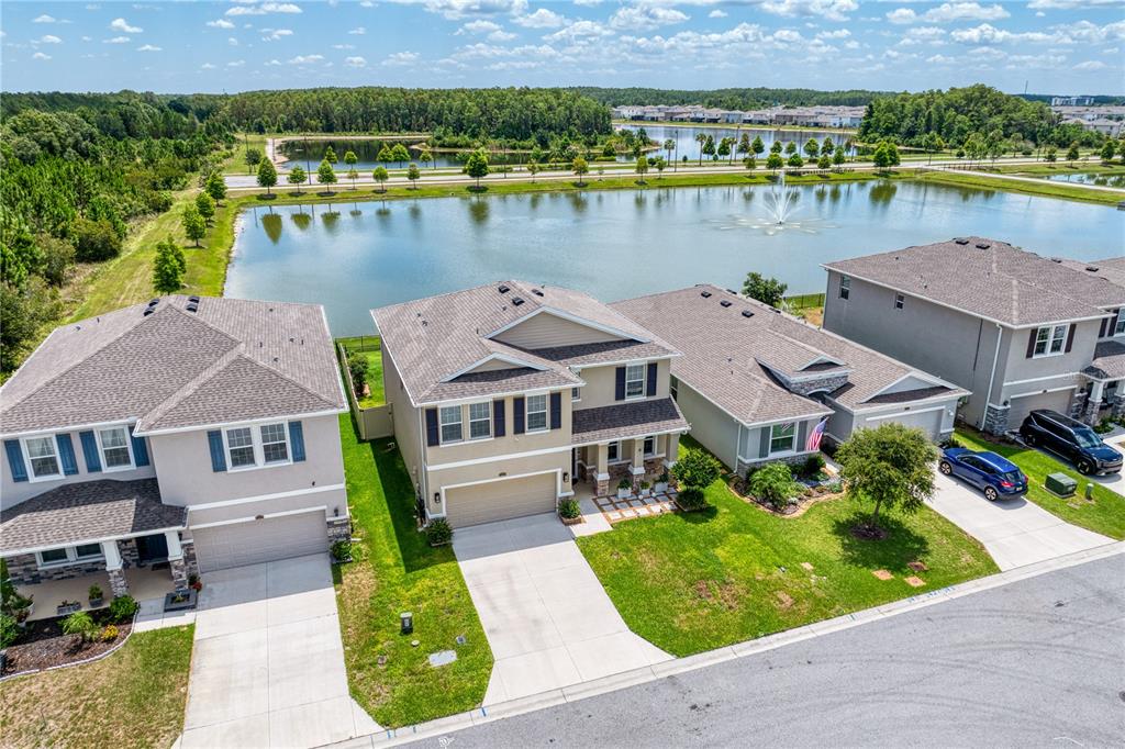 An aerial view shows three suburban houses with driveways facing a pond with a fountain — 3288 TUCSON WIND PLACE, ODESSA, FL