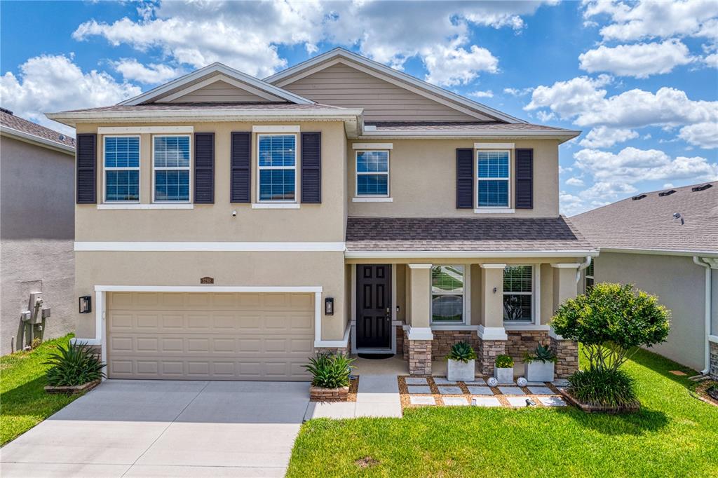 A two-story suburban house features a tan stucco exterior, a two-car garage, and stone accents — 3288 TUCSON WIND PLACE, ODESSA, FL