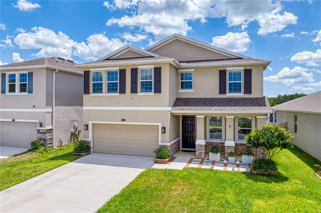 A two-story suburban house with a tan stucco exterior, stone accents, and a two-car garage — 3288 TUCSON WIND PLACE, ODESSA, FL