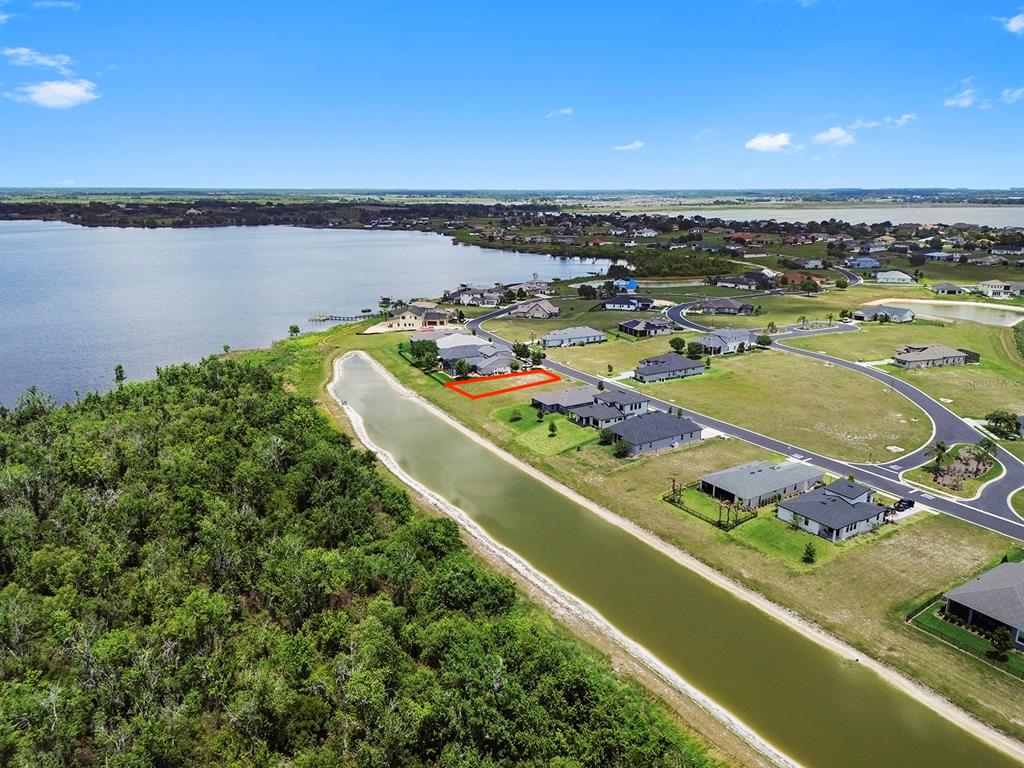 An aerial view shows a vacant residential lot outlined in red next to a canal — 497 ADAMS VIEW LANE, AUBURNDALE, FL