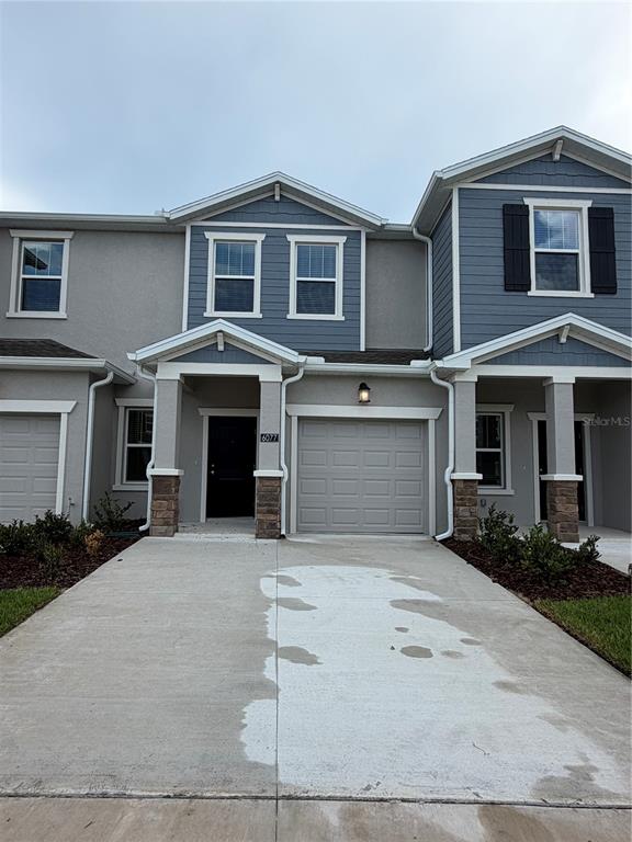 A two-story townhouse exterior features a gray stucco facade, blue siding, and a concrete driveway — 6077 ZEN WAY, CLERMONT, FL