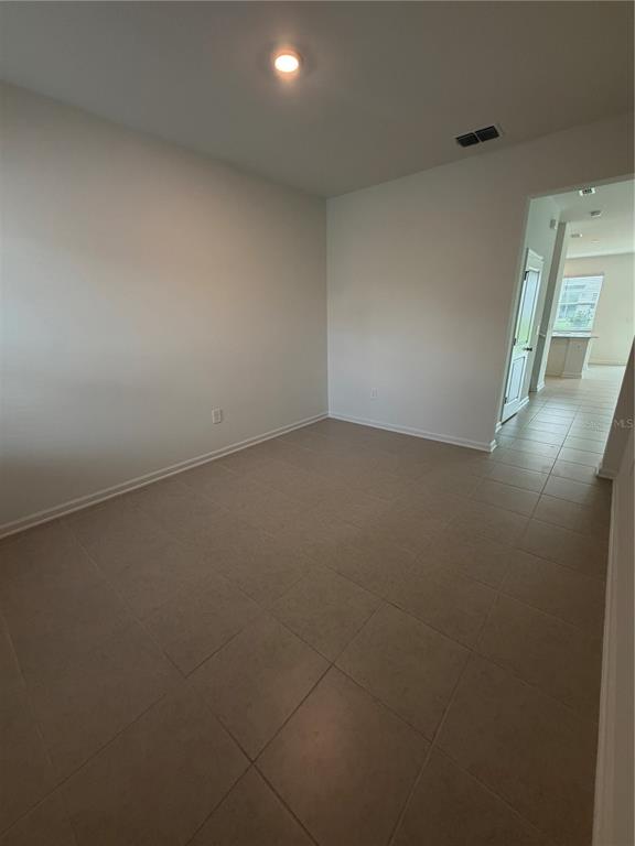 An empty room with light-colored walls and tan tile flooring leads to a hallway — 6077 ZEN WAY, CLERMONT, FL
