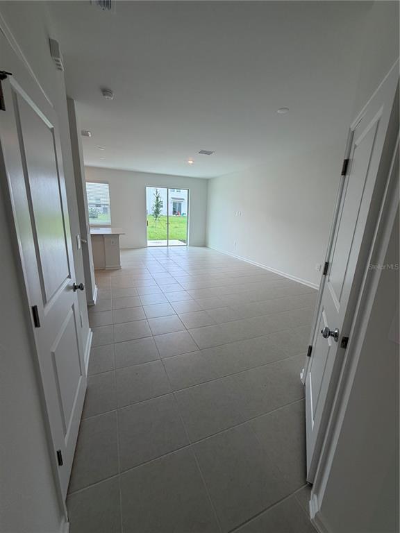 An interior view of a tiled living area with a kitchen island and sliding glass doors — 6077 ZEN WAY, CLERMONT, FL