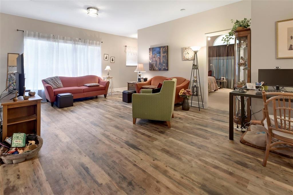 A living room features wood-look flooring, a red sofa, a green armchair, and a desk — 207 VICTORIA COMMONS BOULEVARD, DELAND, FL