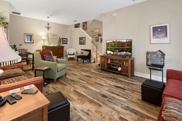 A living room features wood-look flooring, a television on a wooden stand, and various seating — 207 VICTORIA COMMONS BOULEVARD, DELAND, FL
