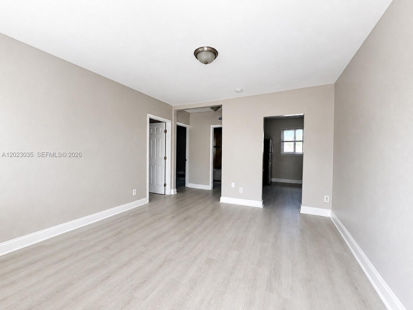 An empty room features light gray walls, wood-look flooring, and multiple doorways leading to other areas — 1920 Washington Ave # 5, Opa-Locka FL 33054, OPA-LOCKA, FL