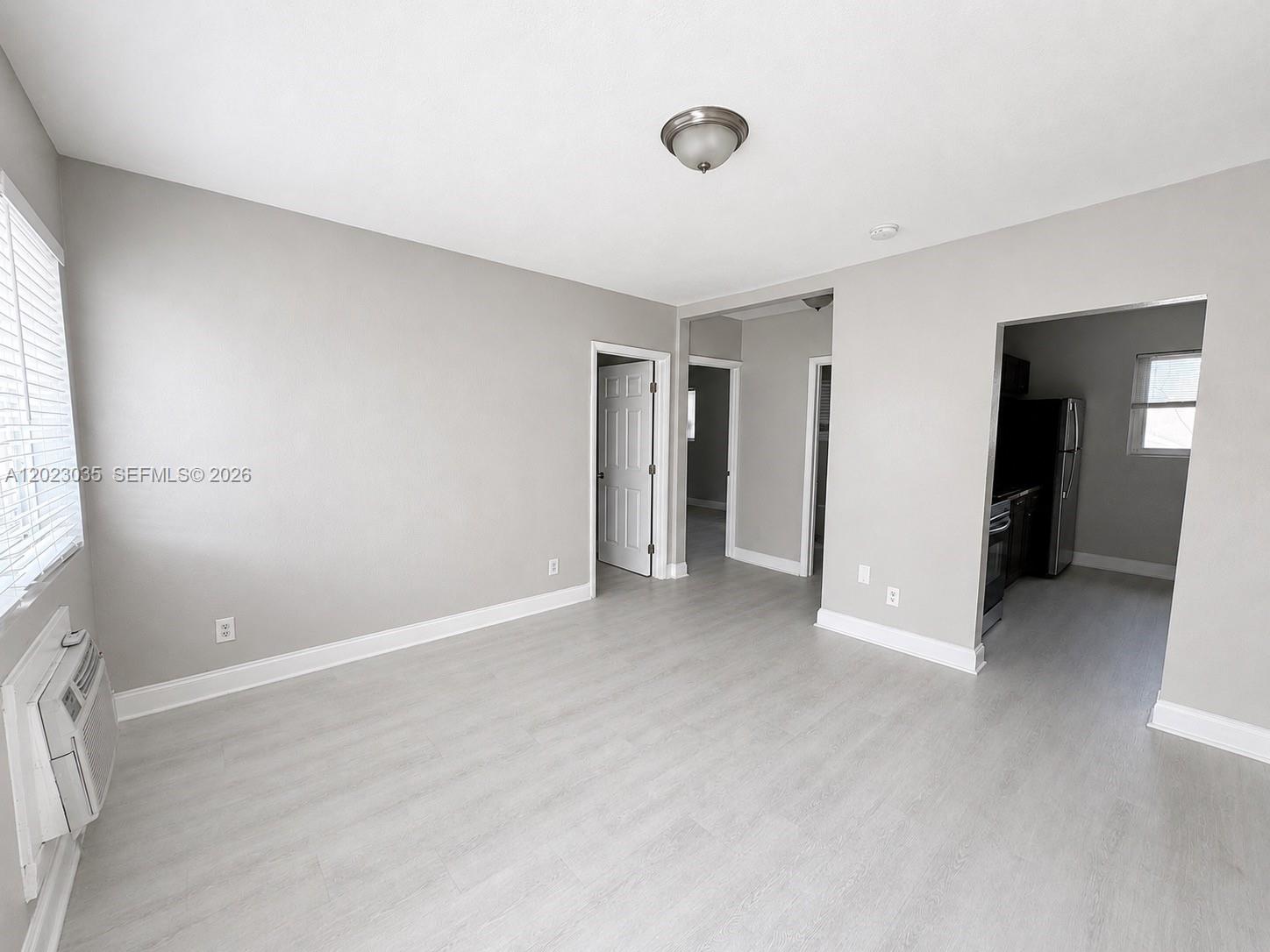 A living room with light gray walls, wood-look flooring, and an adjacent kitchen area — 1920 Washington Ave # 5, Opa-Locka FL 33054, OPA-LOCKA, FL