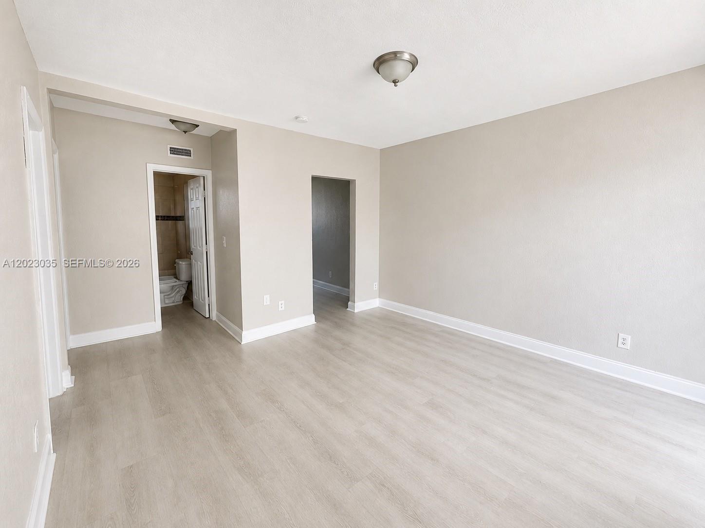 An empty room features light-colored wood-look flooring, beige walls, and two doorways leading to other areas — 1920 Washington Ave # 5, Opa-Locka FL 33054, OPA-LOCKA, FL