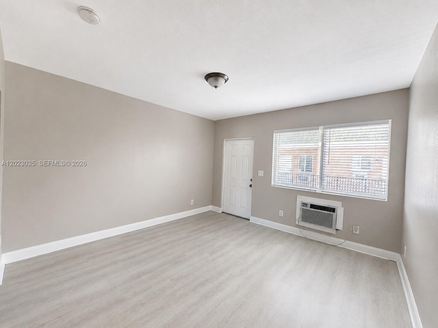 An empty room features light gray walls, wood-look flooring, a window air conditioner, and blinds — 1920 Washington Ave # 5, Opa-Locka FL 33054, OPA-LOCKA, FL