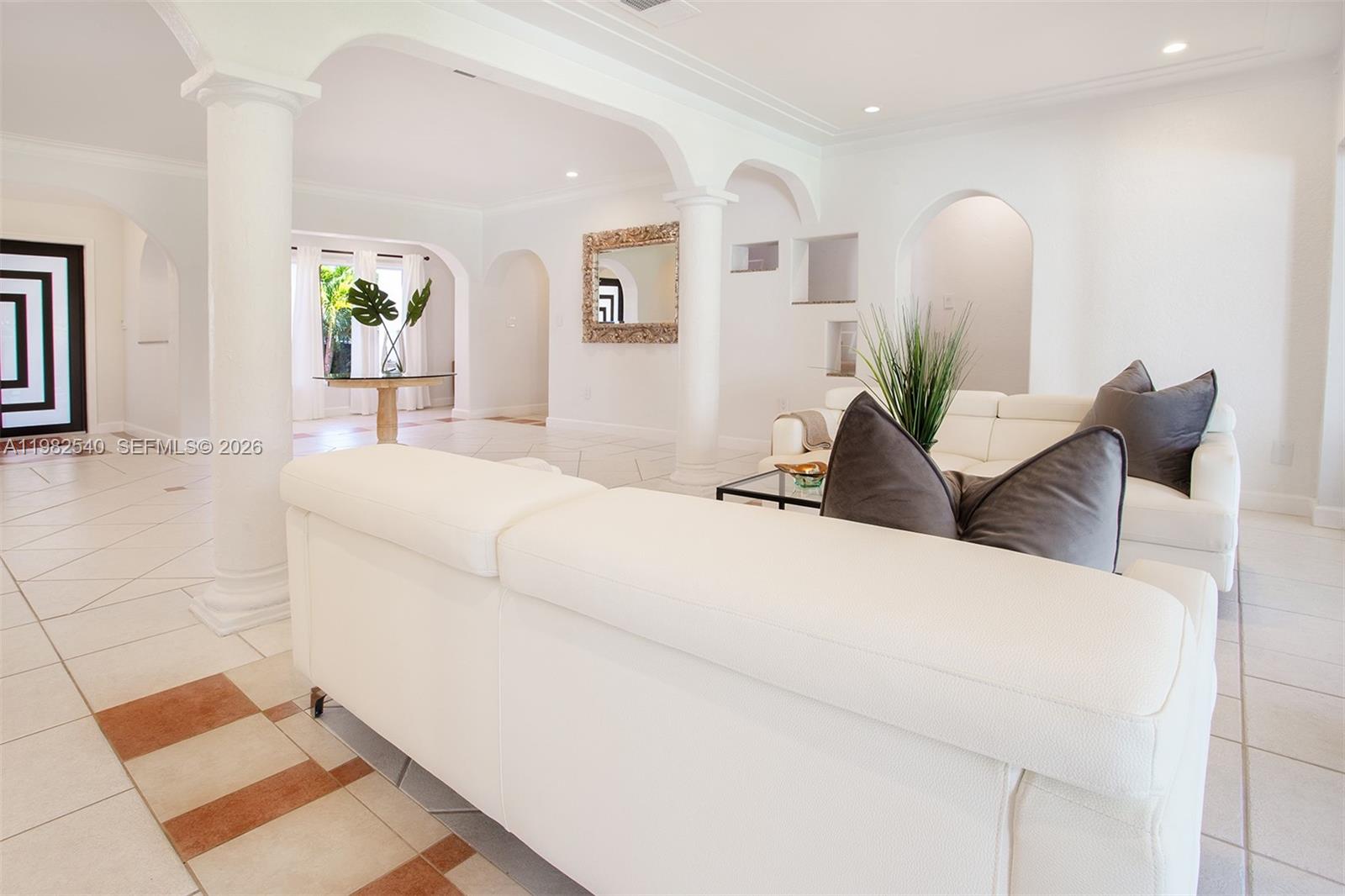 A bright living room features white leather sofas, arched doorways, columns, and tiled flooring — 100 SW 26th Rd, Miami FL 33129, MIAMI, FL