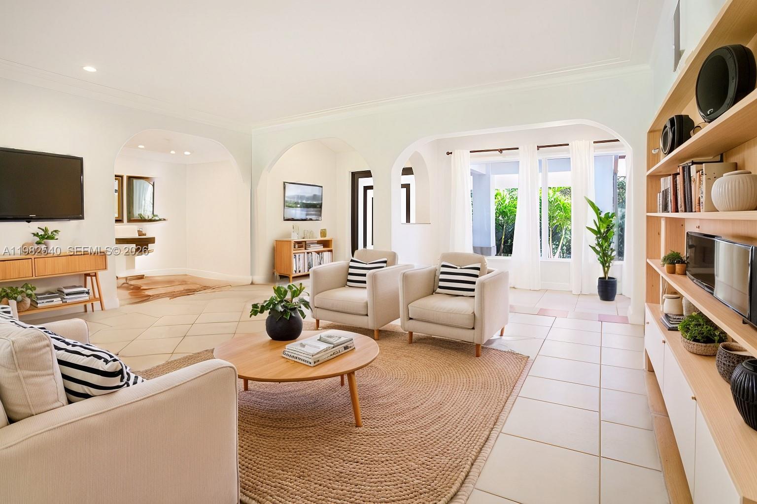 A bright living room features arched doorways, tile flooring, a jute rug, and built-in shelving — 100 SW 26th Rd, Miami FL 33129, MIAMI, FL