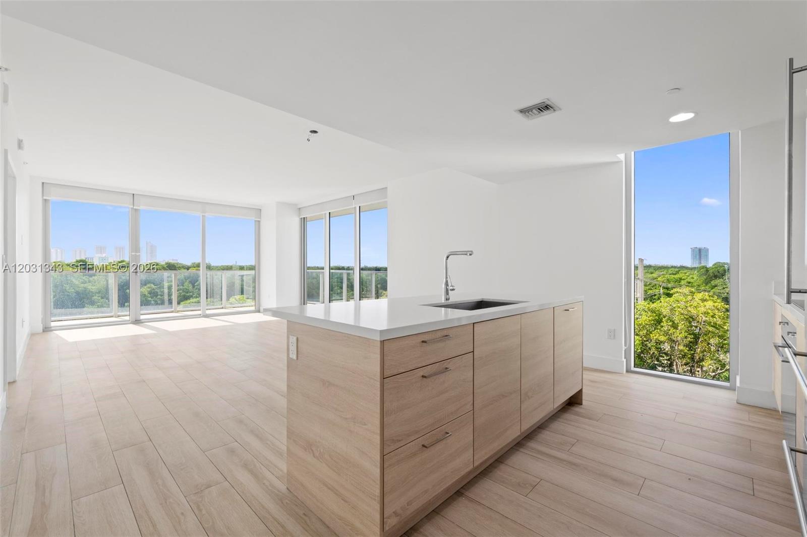 A modern kitchen island with light wood cabinets sits in an open-concept room with floor-to-ceiling windows — NORTH MIAMI BEACH, FL