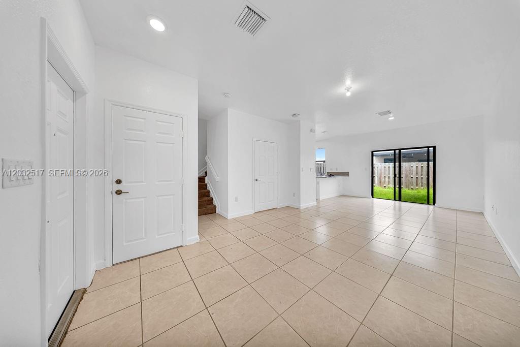 An open-concept living area features light tile flooring, white walls, and a sliding glass door — 23130 SW 127th Ct, Miami FL 33170, MIAMI, FL