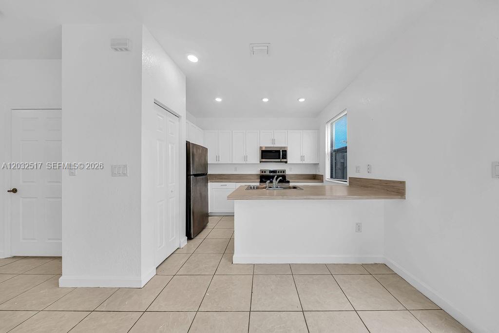 A kitchen features white cabinets, stainless steel appliances, and a peninsula with a wood-look countertop — 23130 SW 127th Ct, Miami FL 33170, MIAMI, FL
