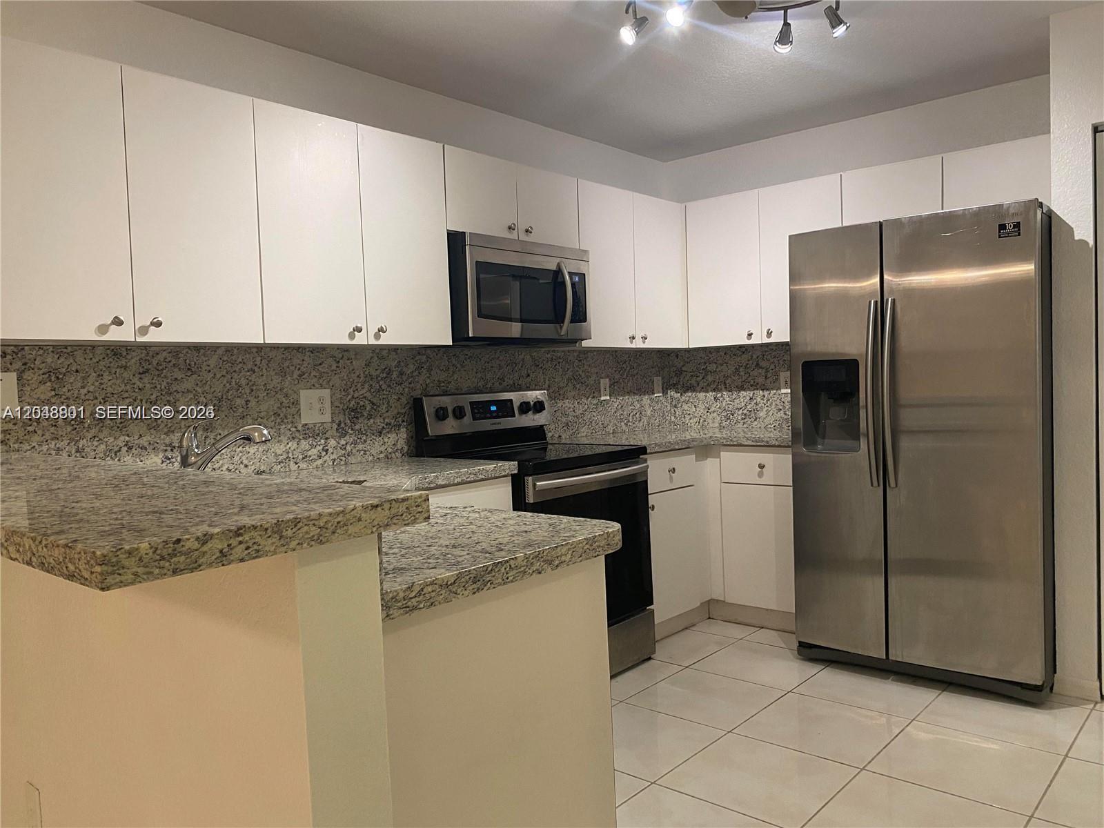 A kitchen features white cabinets, granite countertops, and stainless steel appliances — 11301 SW 17th Ct, Miramar FL 33025, MIRAMAR, FL