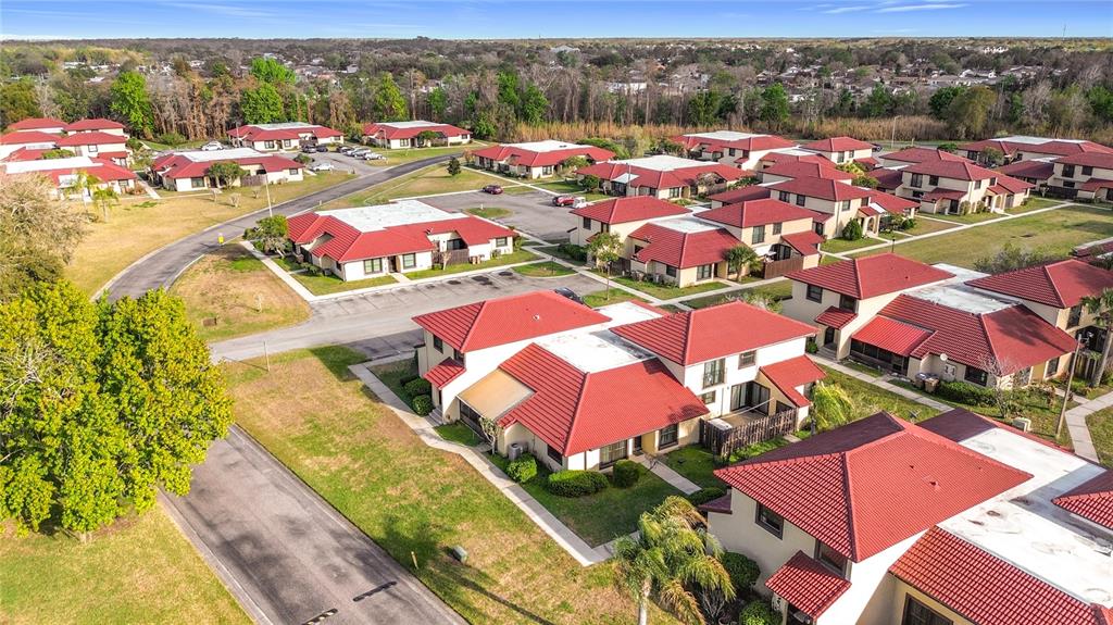 An aerial view shows multiple residential buildings with red tile roofs and surrounding green lawns — 571 HUNTER CIRCLE, KISSIMMEE, FL