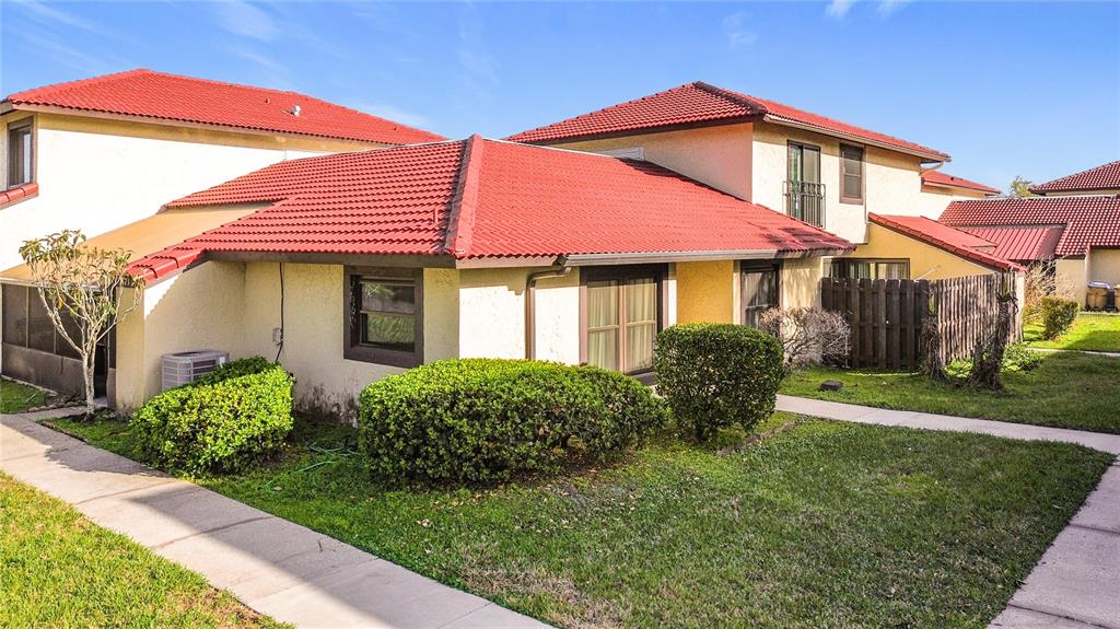 A tan stucco townhouse features a red tile roof and a small front lawn — 571 HUNTER CIRCLE, KISSIMMEE, FL