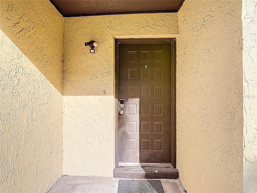 A brown front door with a keypad lock is set into a textured stucco wall — 571 HUNTER CIRCLE, KISSIMMEE, FL