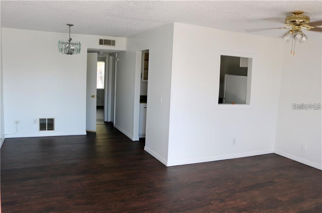 A living room with dark wood-look flooring, white walls, a ceiling fan, and a pass-through window — 9101 W HILLSBOROUGH AVENUE UNIT I207, TAMPA, FL