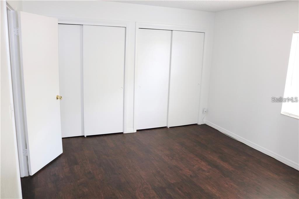 A bedroom features dark wood-look flooring, white walls, and two sets of sliding closet doors — 9101 W HILLSBOROUGH AVENUE UNIT I207, TAMPA, FL
