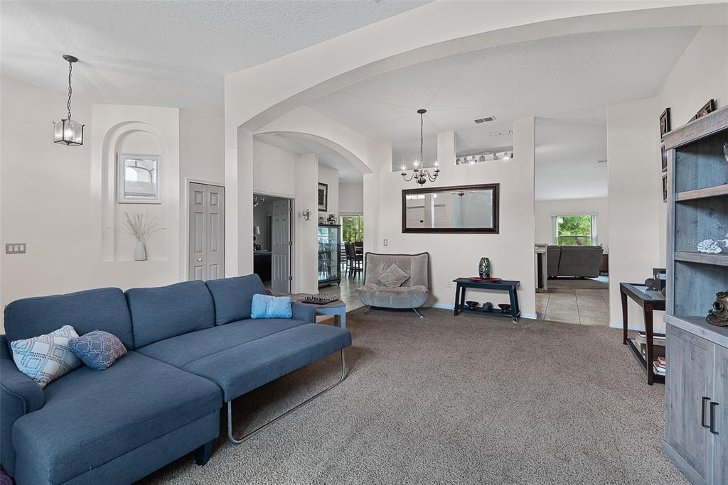 A living room features a blue sectional sofa, beige carpet, and arched architectural wall openings — 3 RUSSMAN LANE, PALM COAST, FL