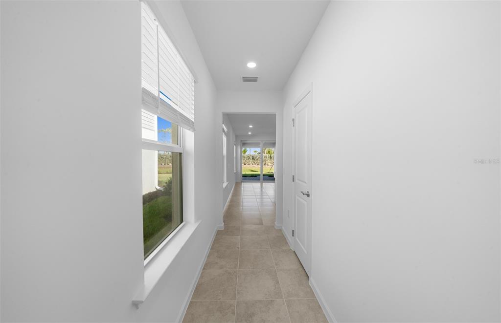 A bright hallway with white walls, tile flooring, and a window overlooking a grassy yard — 813 BALLEBY TRAIL, BRADENTON, FL