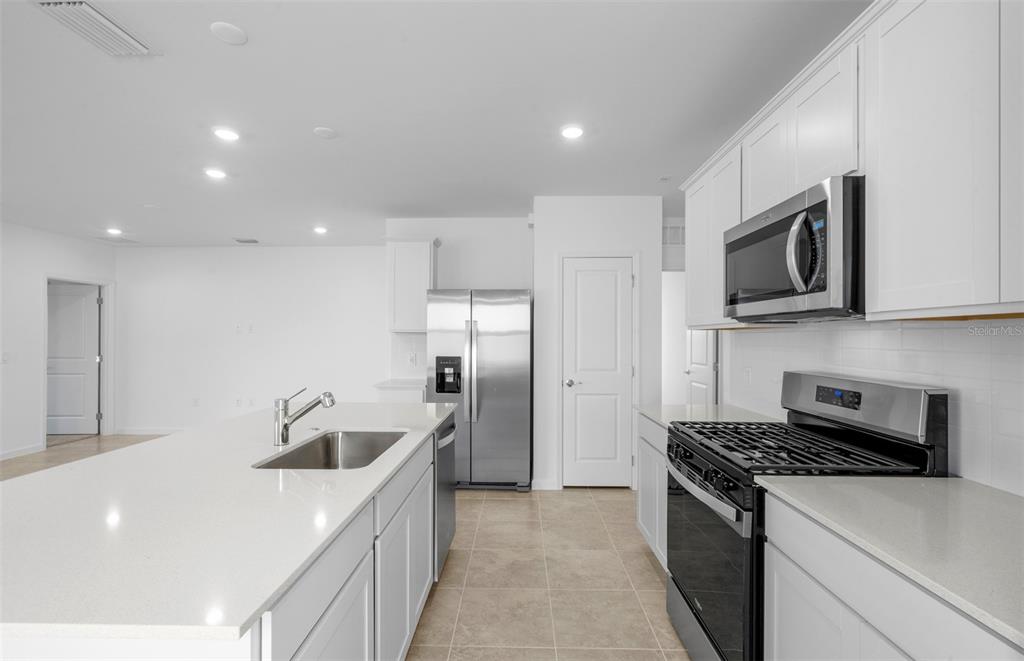 A modern kitchen features white cabinetry, stainless steel appliances, and a large quartz island — 813 BALLEBY TRAIL, BRADENTON, FL