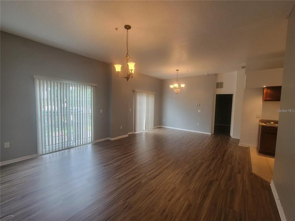 An open-concept living and dining area features wood-look flooring, two chandeliers, and sliding glass doors — 1432 BROKEN OAK DRIVE UNIT 31A, WINTER GARDEN, FL