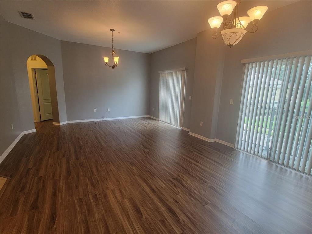 An empty living room features wood-look flooring, gray walls, two chandeliers, and sliding glass doors — 1432 BROKEN OAK DRIVE UNIT 31A, WINTER GARDEN, FL