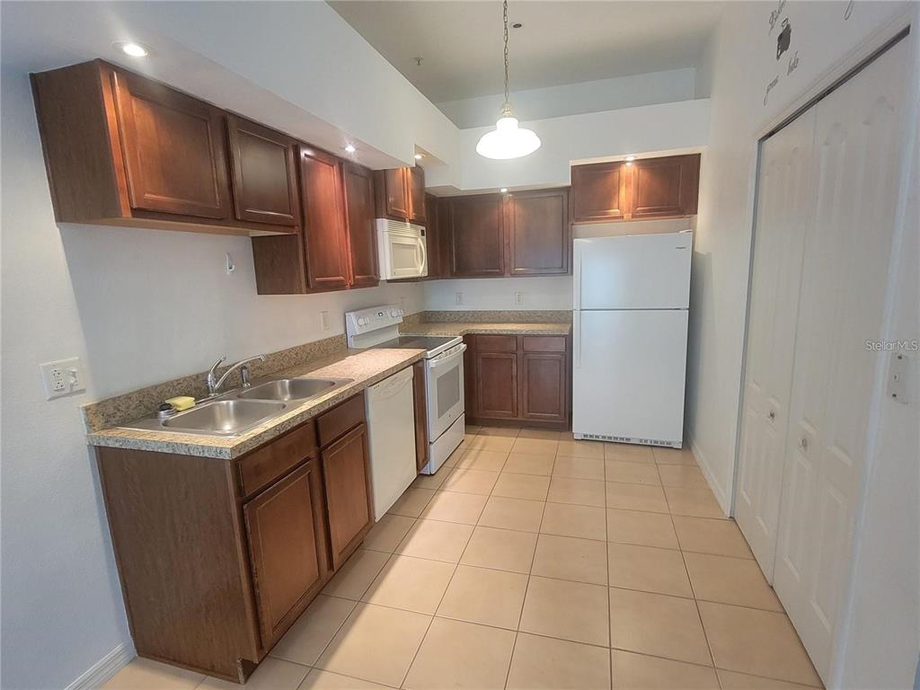 A kitchen features wood cabinets, white appliances, a double sink, and light-colored tile flooring — 1432 BROKEN OAK DRIVE UNIT 31A, WINTER GARDEN, FL