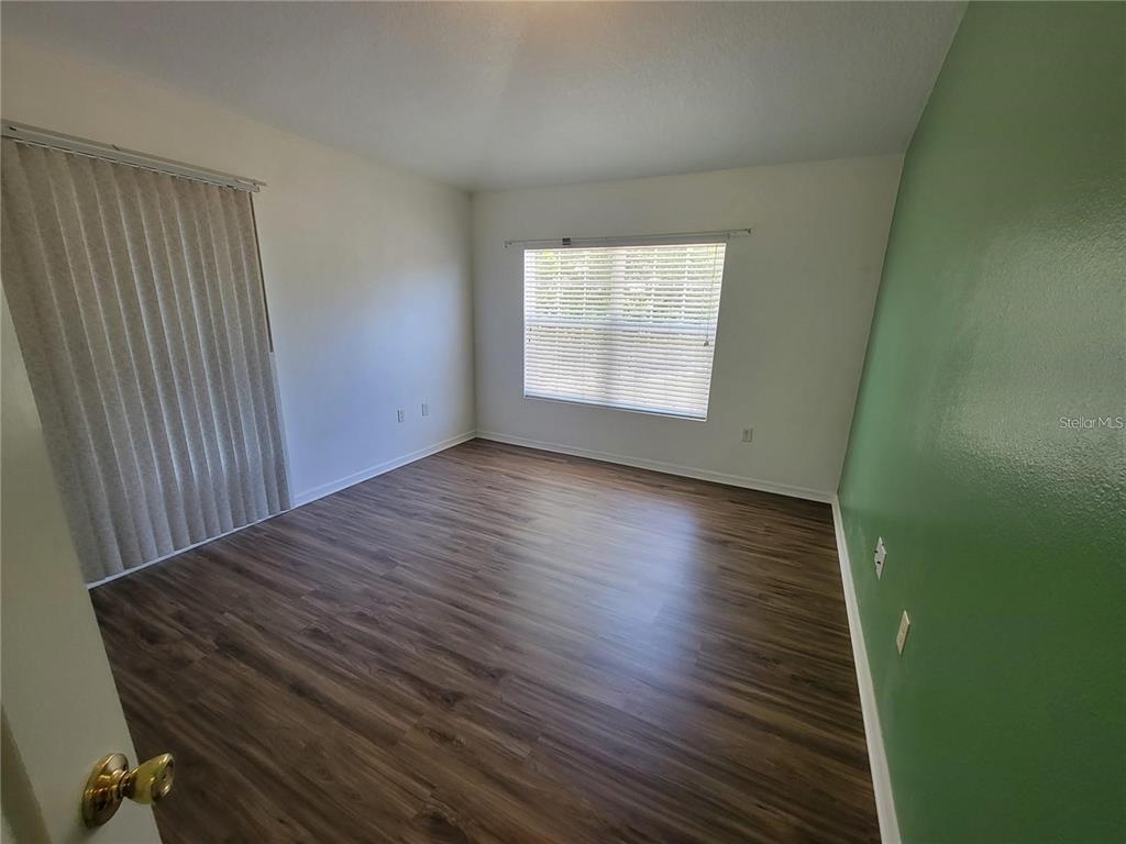 An empty bedroom features wood-look flooring, white walls, a green accent wall, and window blinds — 1432 BROKEN OAK DRIVE UNIT 31A, WINTER GARDEN, FL